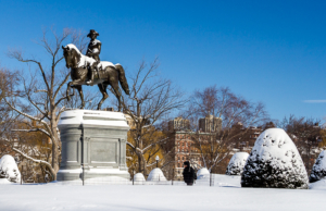 A sunny day in the Boston Public Garden as a pedestrian strolls by George Washington dusted with snow
